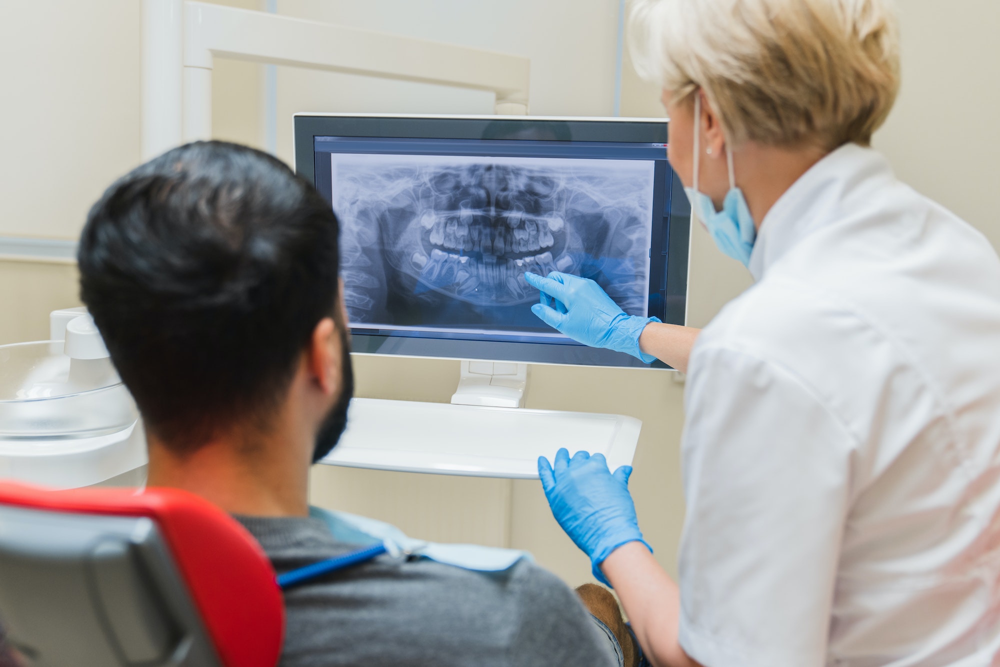 Dentist showing x-ray photo of jaws on computer screen to a male patient in dental clinic.