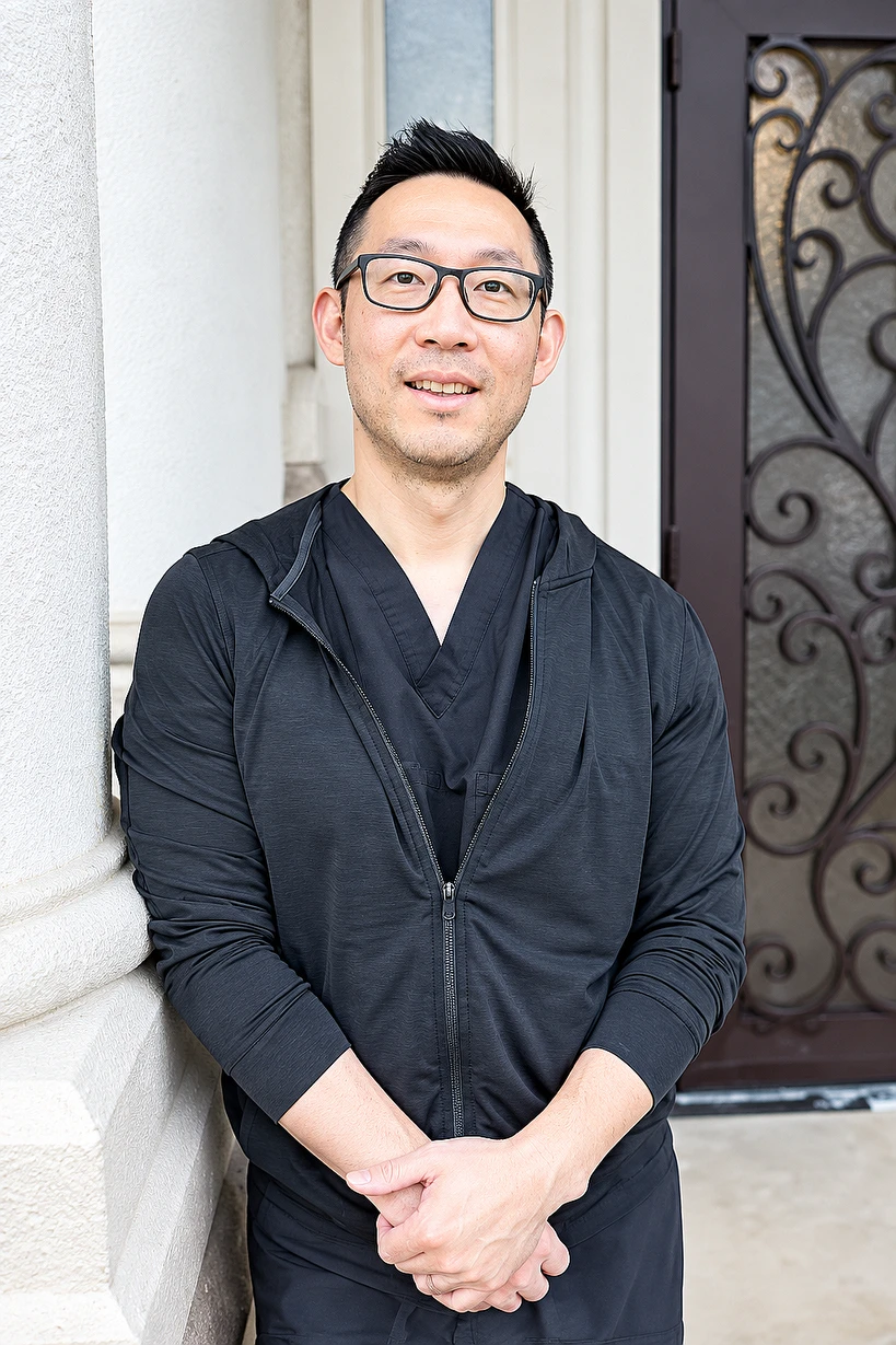Dr. Bobby Kwon in dark scrubs and glasses, standing by a stone column