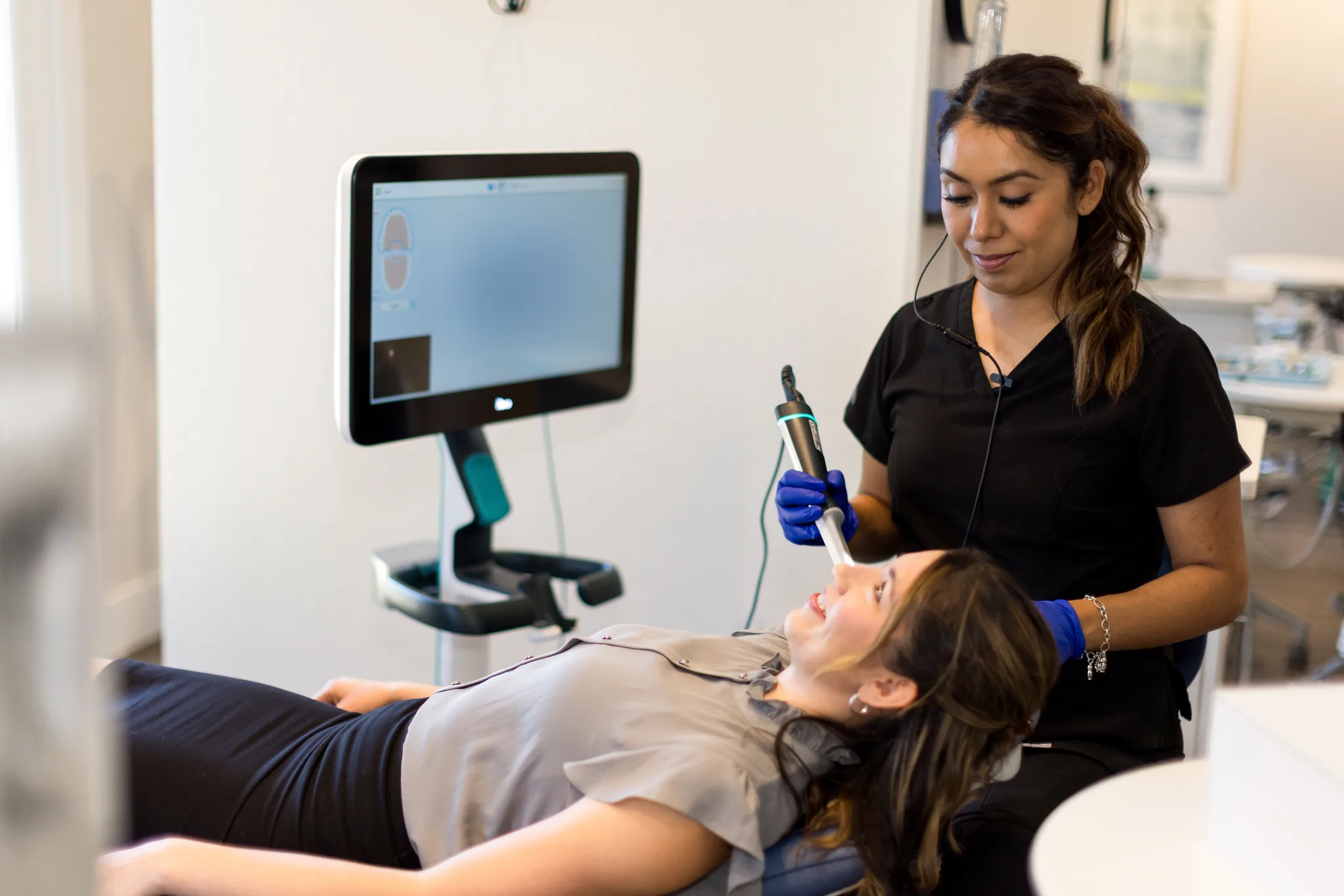 A dental assistant passing an intraoral scanner over a patient's teeth while the 3D model builds on the chairside monitor