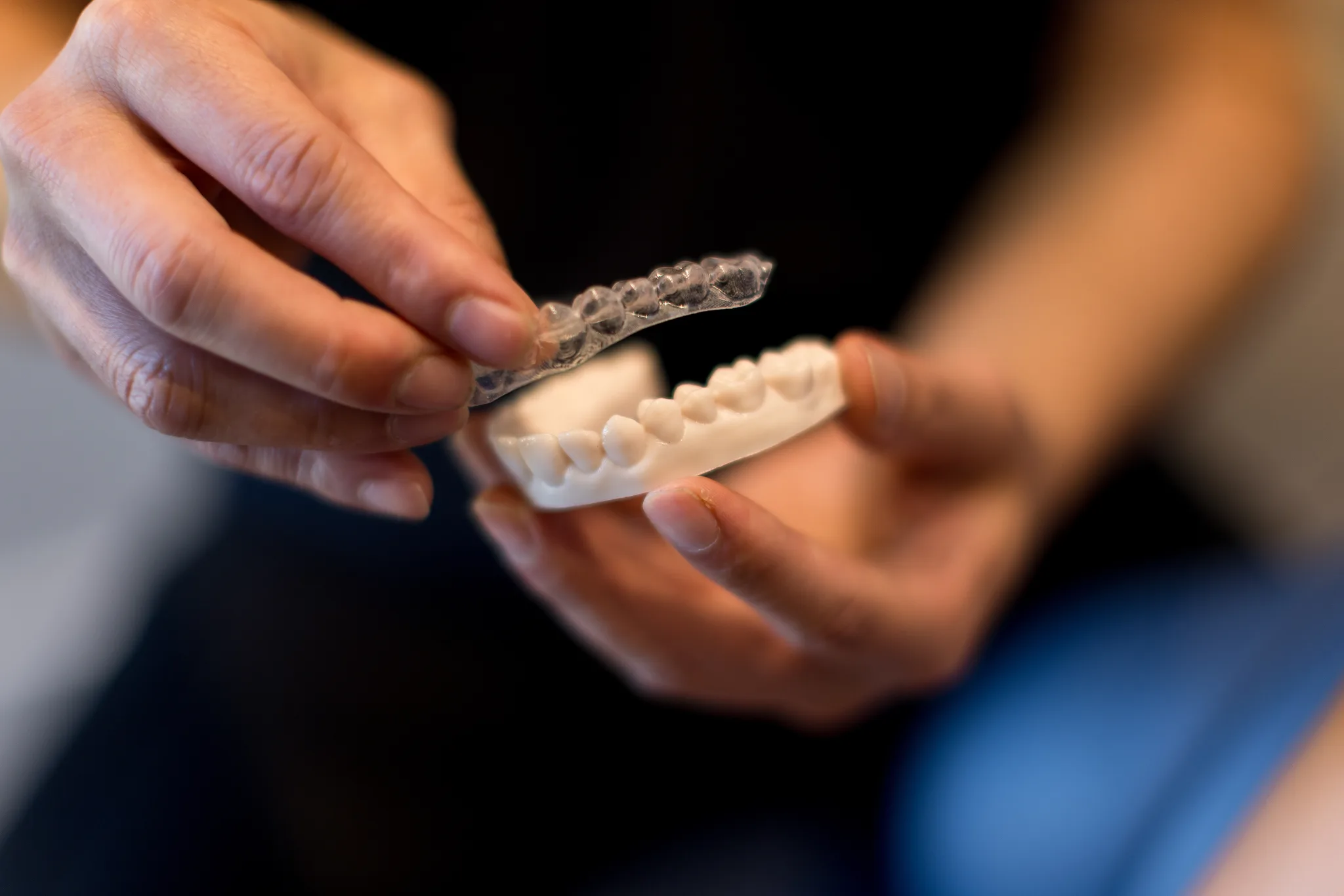 Hands holding a clear aligner above the matching dental model