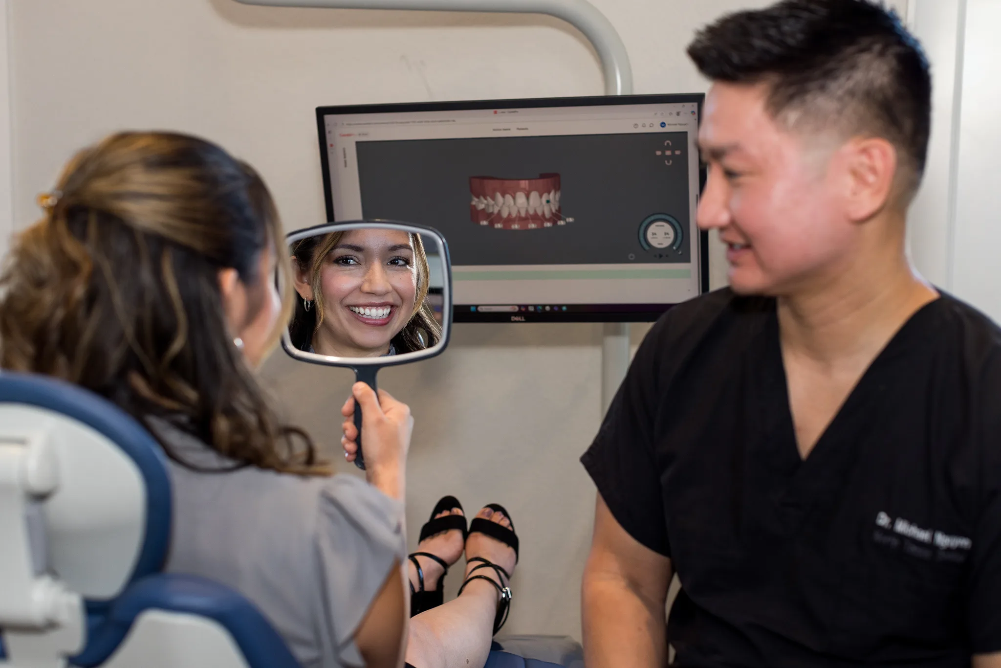 A patient seeing her smile in a hand mirror while the digital smile design shows on the monitor