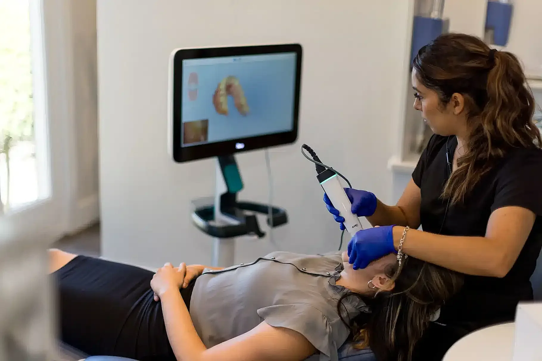 Clinician using an intraoral scanner while a 3D tooth model shows on screen
